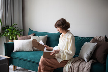 woman girl opens online order purchase cardboard box sitting at home on sofa. concept of buying through an online store