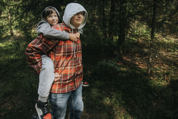 Two people walking in a forest, one giving the other a piggyback ride, both dressed in hoodies and...
