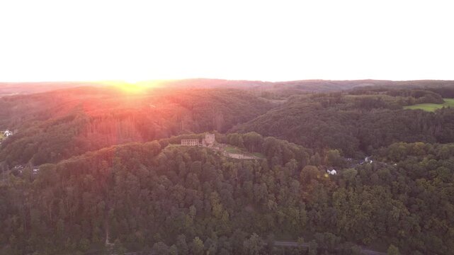Distant drone orbit around Windeck Castle ruins on a hill in North Rhine-Westphalia, Germany, with rolling hills and scenic sunset horizon in the background, cinematic landscape view