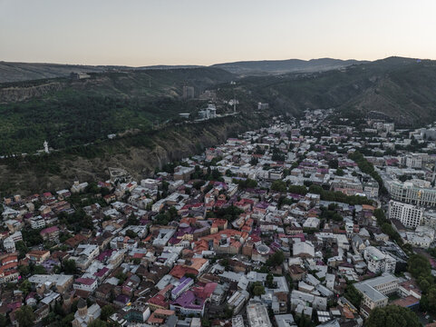 Aerial view of terracotta rooftops cascading down the hills towards the city center, with the Narikala Fortress perched on a distant ridge, Tbilisi, Tbilisi, Georgia.