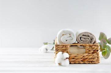 Rolled towels in straw basket decorated with cotton flowers on empty space table. Bathroom...