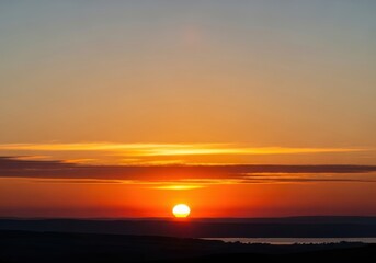Fototapeta premium Vibrant sunset over the horizon with colorful sky and clouds, casting a warm glow on the landscape below