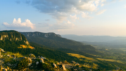 Mountain ridge and steep rocky slopes illuminated by sunset, with panoramic views across green...