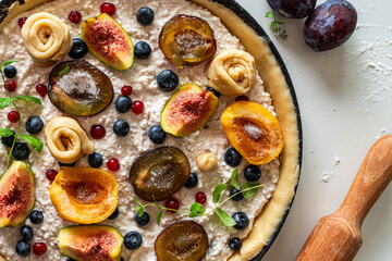 Raw tart or open summer pie with figs, prunes, apricots and blueberries is ready to bake in a round mold. Close-up. View from above.