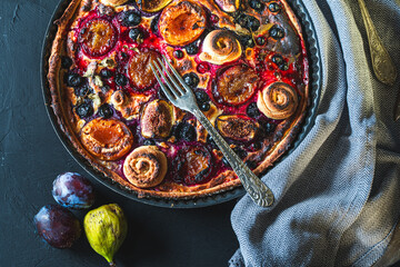 A tart or open pie with blueberries, figs, prunes and apricots in a baking dish on a gray background with a fork and napkin on the table. Top view