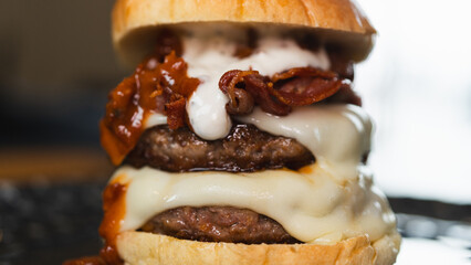 Massive gourmet burger with two juicy beef patties, overflowing melted cheese, crispy bacon, rich...