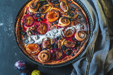 A tart or open pie with blueberries, figs, prunes and apricots in a baking dish on a gray background. Close-up. High quality photo