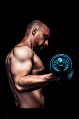 Shirtless muscular man curling dumbbell in dark studio lighting