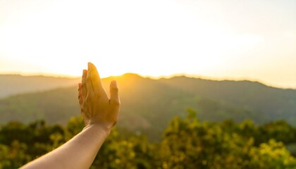A hand reaches towards a golden sunset over a hazy mountain range, evoking a sense of peace and connection with nature.