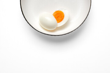 Clean overhead shot of a whole egg beside a halved hard-boiled egg on a white plate. The high-key background and generous copy space suit ads, recipe cards, and nutrition articles.