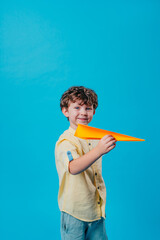Little boy holding paper plane standing over blue background