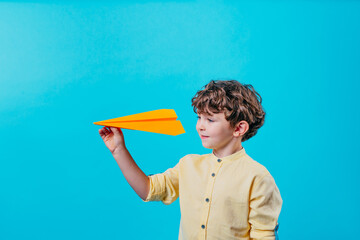 Little boy holding paper plane standing over blue background
