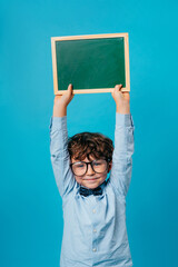 Happy preschool boy wearing bow tie holding chalk board over blue background