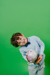 Happy preschool boy looking at the globe through a magnifying glass standing over green background