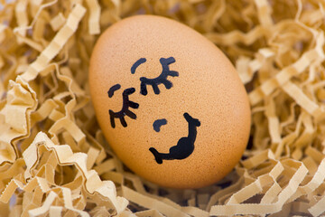 An adorable brown egg with a smiling face, snuggled in soft, colorful shredded paper decoration...