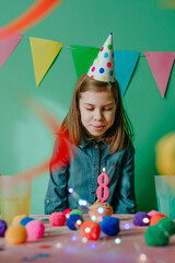 Little girl wearing birthday hat blowing on the candle on cupcake