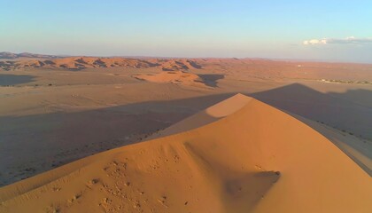 A vast, sun-drenched desert landscape showcases a towering sand dune, its golden hues highlighting the dramatic terrain.