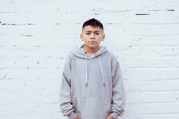 Latin boy standing with hands in pockets against white wall