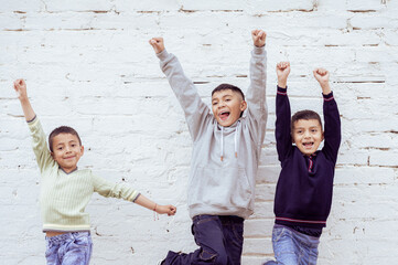 Three latin american children celebrating with raised fists in front of white brick wall