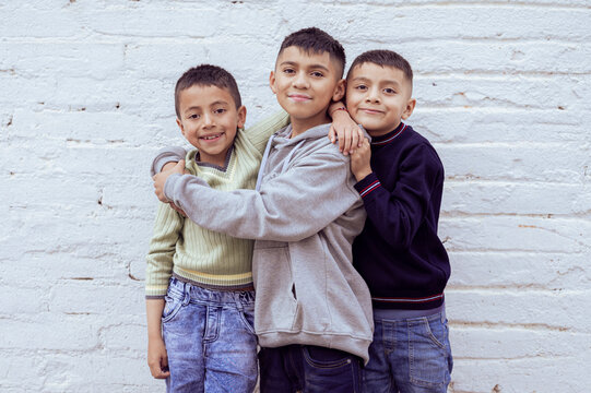 Three latin american brothers hugging and smiling in front of white wall