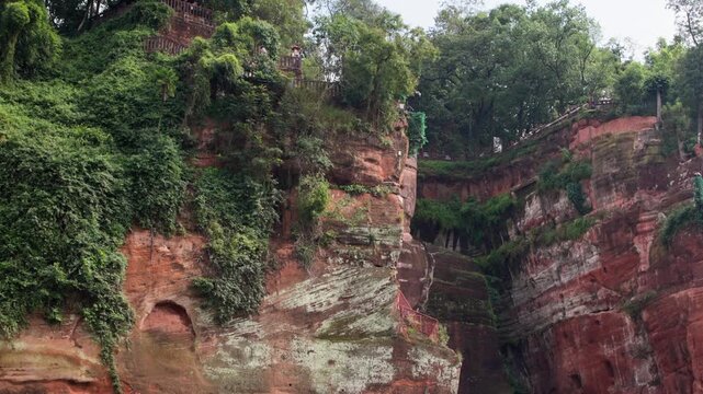 Wide slow motion shot of the entire Leshan Buddha from side angle, showing scale and surrounding natural context