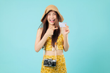 Young asian woman hold card credit travel summer pointing vacation payment, wearing a straw hat and holding a camera, she points her finger to the card, headshots isolated studio blue background
