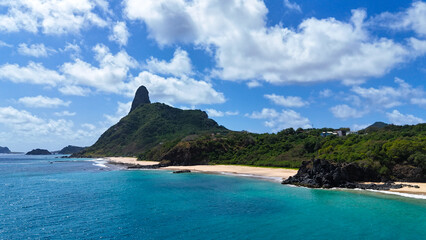 Imagem aérea da Praia do Americano em Fernando de Noronha, com o Morro do Pico ao fundo e o contraste entre o mar azul e as falésias, destacando a natureza intocada da ilha © RNL Fotografia