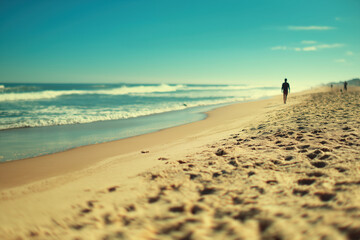 Obraz premium Walking along a sandy beach with gentle waves under a clear blue sky