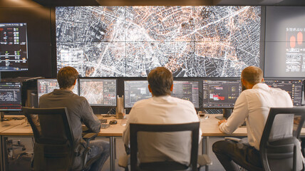 Team in a control room watches a large digital city screen; analytics, monitoring and technical atmosphere.