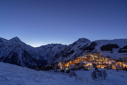 Twilight alpine village lights against snow-covered mountainside