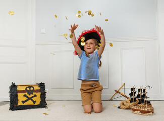 Young pirate child tosses a handful of coins by treasure chest