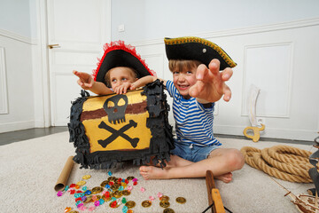 Two kids in striped shirts hug pirate chest amid scattered coins