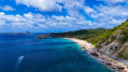 Vista aérea de praia paradisíaca em Fernando de Noronha, com mar azul cristalino, falésias verdes e faixa de areia clara formando paisagem tropical preservada