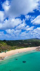 Aérea de praia tropical em Fernando de Noronha com mar turquesa, encostas rochosas e vegetação densa ao redor, exibindo beleza natural preservada