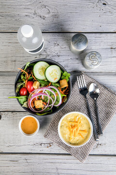 Salad with a bowl of cream of broccoli soup with shredded cheddar cheese and a bottle of water 