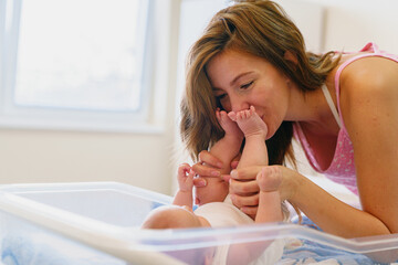 Young Caucasian Mother Kissing Her Newborn's Feet in a Bright and Serene Indoor Setting