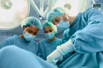 Diverse Medical Team Performing Surgery Under Operating Room Lights With Surgical Masks And...