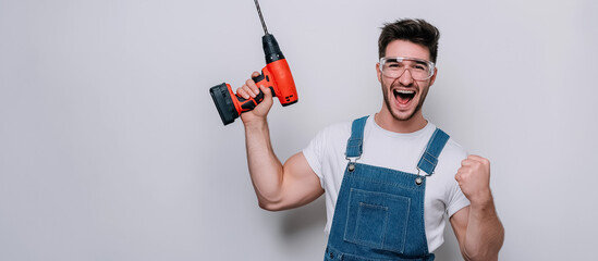 handyman in denim overalls and safety glasses, holding a drill and celebrating success. An ideal image for DIY blogs, home improvement advertisements, or tools and equipment promotions.