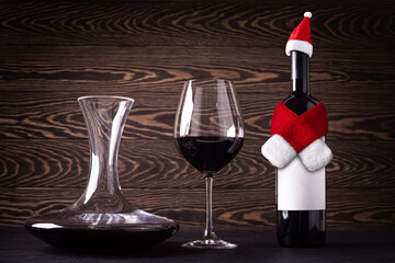 Decanter, glass and santa claus hat and scarf on bottle with red wine on wooden rustic background....