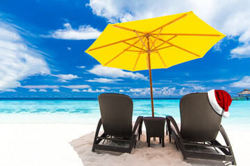 Santa Claus hat on sunbed on tropical beach with sun umbrellas and chaise longues. Christmas and...