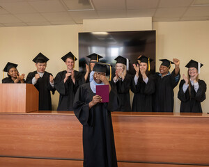 Happy African woman in hijab receiving diploma and classmates applauding her. 