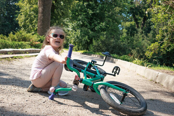 Little girl sitting on path after falling off bicycle