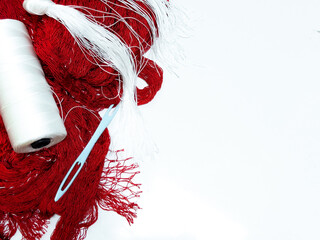 Red yarn and white thread with blue needle on white background