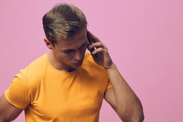 young man talking phone in orange t-shirt on pink background communication digital nomad technology...