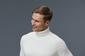 Smiling man dressed in white knitted sweater looking to the side against gray background, portrait...