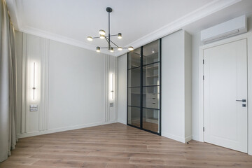 A spacious, bright room with wall lamps, a modern chandelier and a built-in wardrobe with sliding glass doors. Unfurnished.