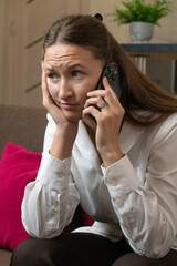 Sad businesswoman sitting in her home office, holding her head in her hands while listening to...