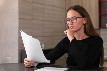 Young businesswoman wearing glasses, reading through important documents and thoughtfully resting...