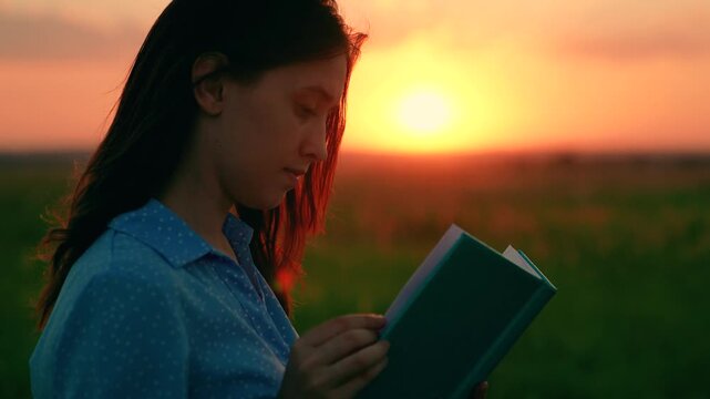 Young woman reads book in autumn park in rays of sunset. Prayer in nature. Student reads textbook in nature in spring. Man reading book outdoors. Studying, education. Beautiful woman praying at sunset