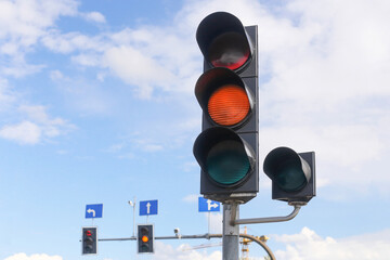 Traffic light with orange signal glowing on city street. Road safety and regulation symbol against blue sky with clouds. Urban transport and driving rules concept. Modern infrastructure and navigation